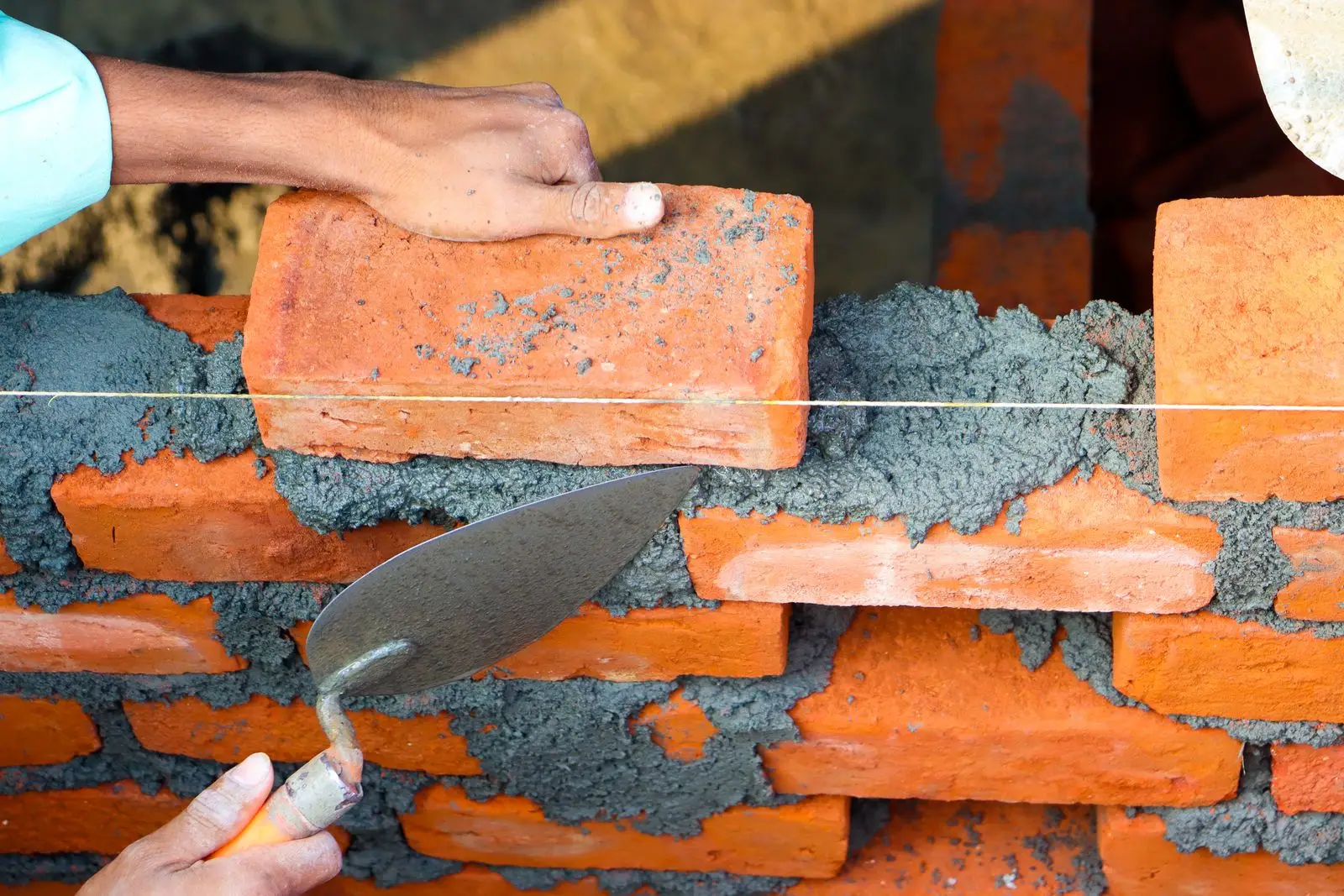 Mason bedding a brick into fresh mortar with a trowel along a line