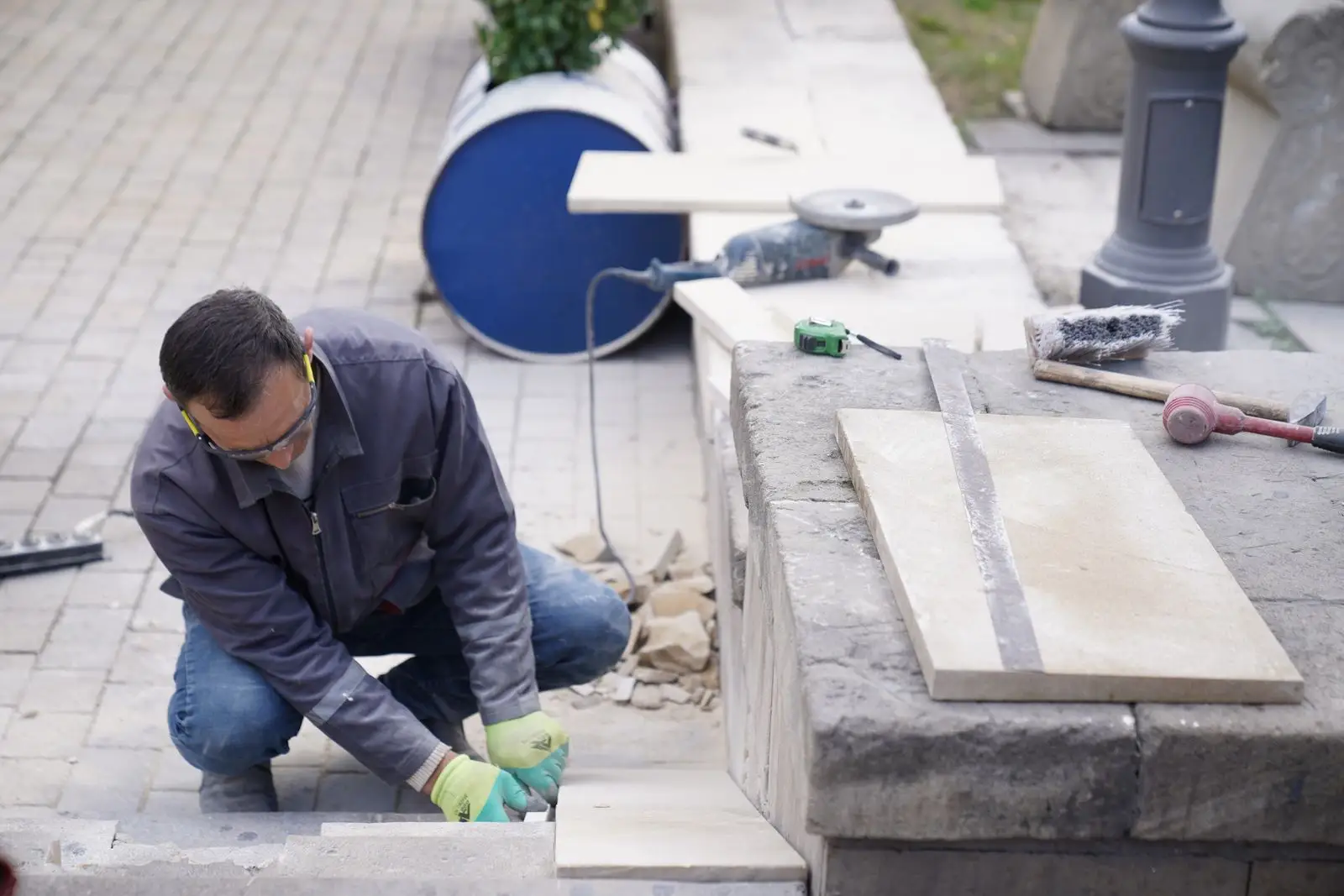 Mason kneeling to set cut stone on a job site, tools laid out beside him