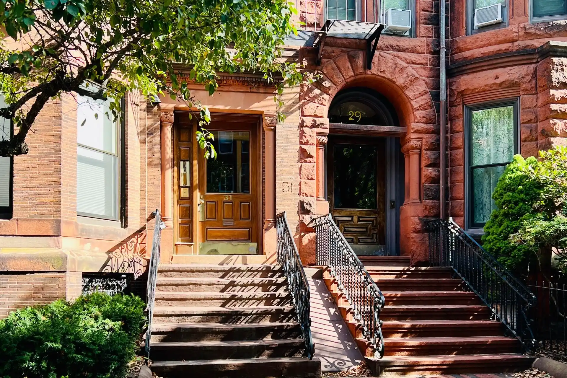 Brownstone facade with stone steps and a brick retaining wall on a sunny street